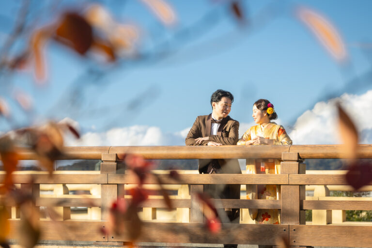 岡山の町並みを背景に、新婦が和装、新郎がタキシード姿で並ぶ前撮り風景