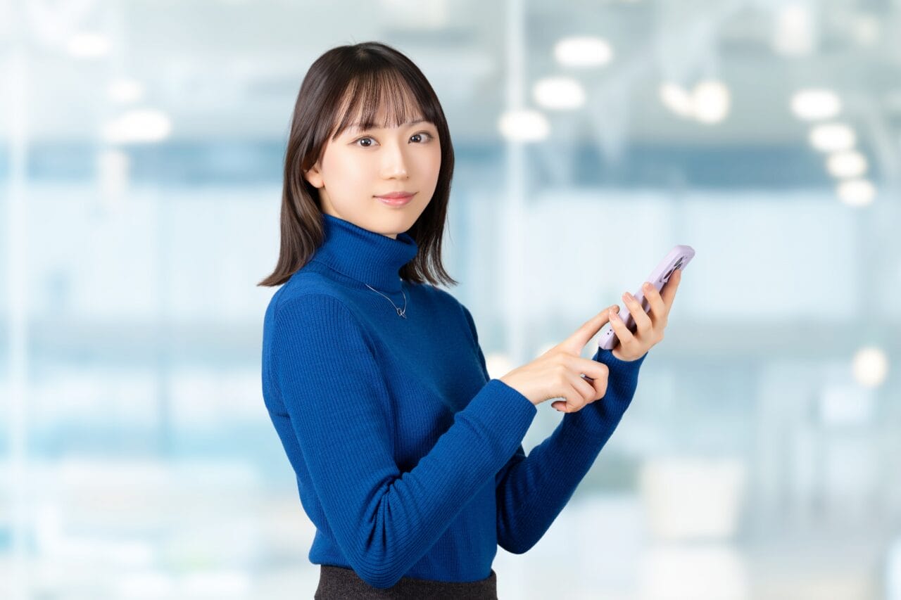 スマートフォンを手に、カメラに向かって静かに微笑む女性