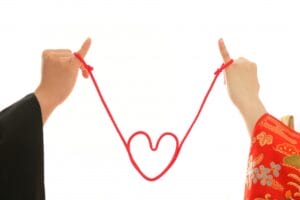 赤い糸で結ばれたふたりの小指がハートを描いている写真