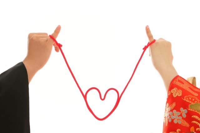 赤い糸で結ばれたふたりの小指がハートを描いている写真
