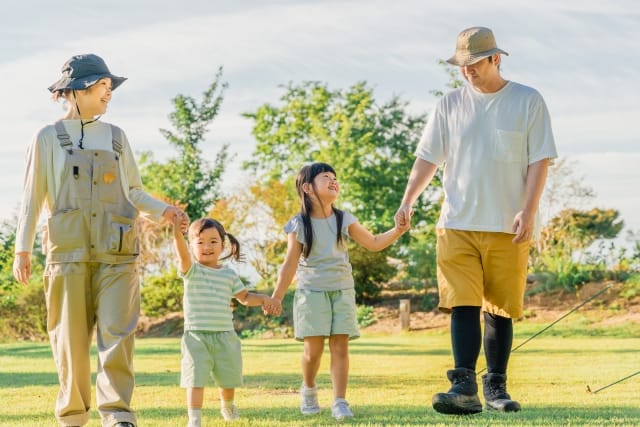 キャンプ場で手をつなぎ、幸せそうに歩く夫婦と子供二人の家族の姿
