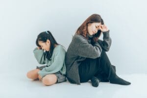 背中を合わせて座り、悩んだ表情を見せる母親と娘の様子