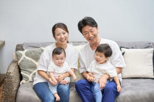 ソファーに座り、子供二人を抱きしめて笑顔を向ける家族の写真｜対話と関係性を大切にする家庭のイメージ