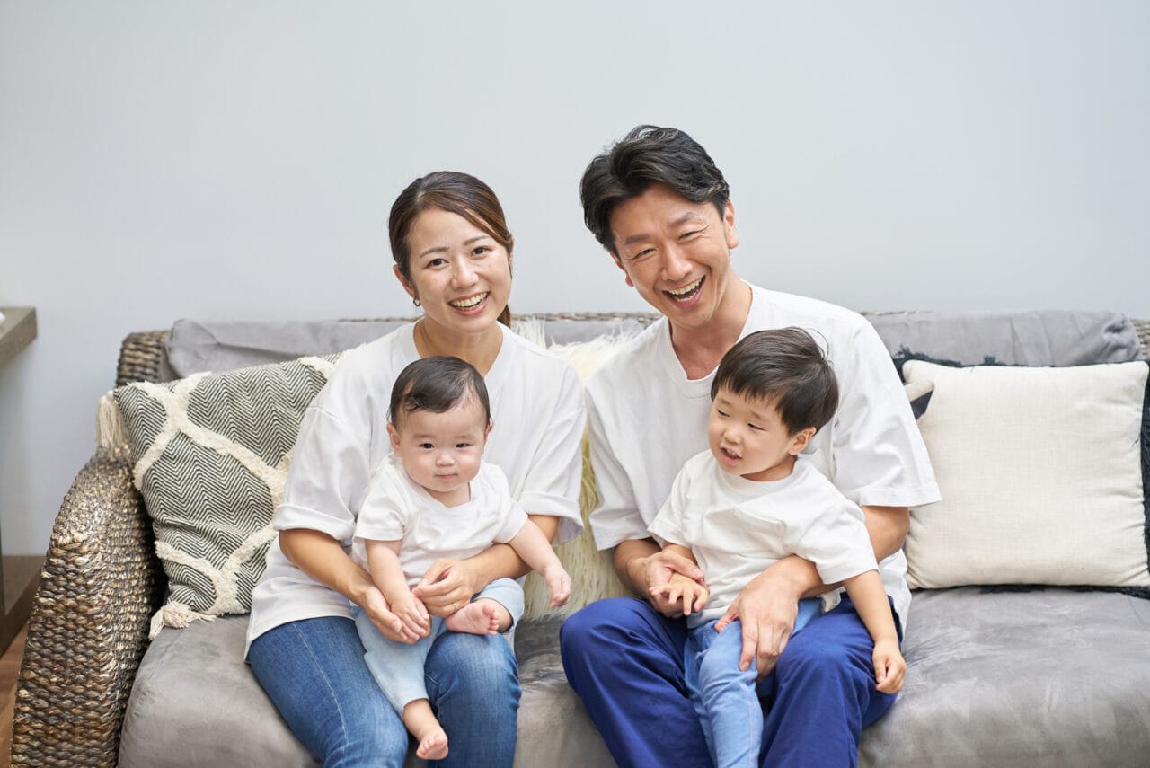 ソファーに座り、子供二人を抱きしめて笑顔を向ける家族の写真｜対話と関係性を大切にする家庭のイメージ