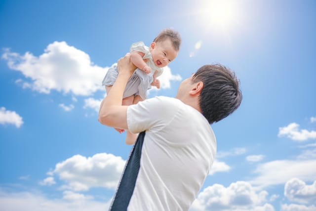 父親が赤ちゃんを高い高いして笑顔を引き出す様子｜安心感のある家庭をイメージした写真