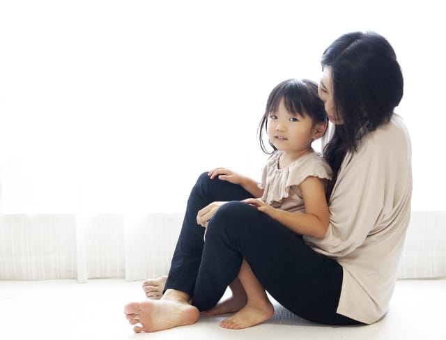 母親が後ろから娘を抱きしめ、安心した表情で寄り添う親子の様子