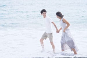 海辺を手をつないで楽しそうに歩くカップル