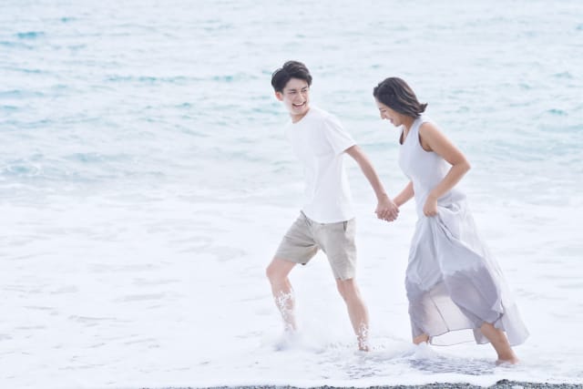 海辺を手をつないで楽しそうに歩くカップル