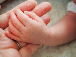 赤ちゃんの小さな手と母親の手が優しくつながる様子。成婚後に新しい家族を迎えた幸せな暮らしを象徴する一枚。