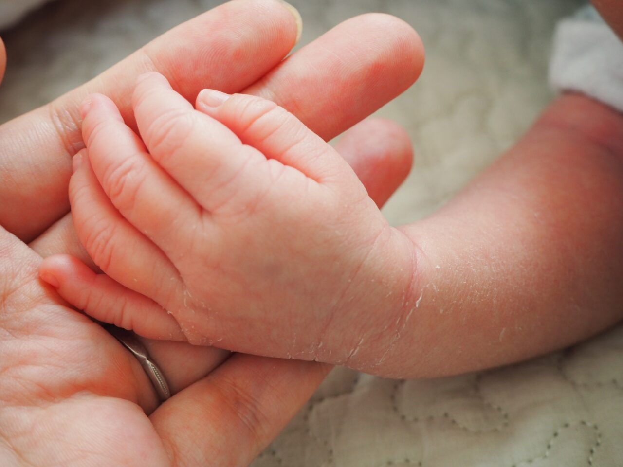 赤ちゃんの小さな手と母親の手が優しくつながる様子。成婚後に新しい家族を迎えた幸せな暮らしを象徴する一枚。
